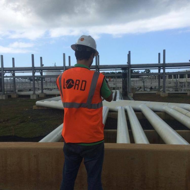 A construction employee surveying a field of industrial piping